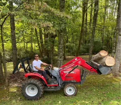 A man is driving a red tractor with removed trees in Durham NC.