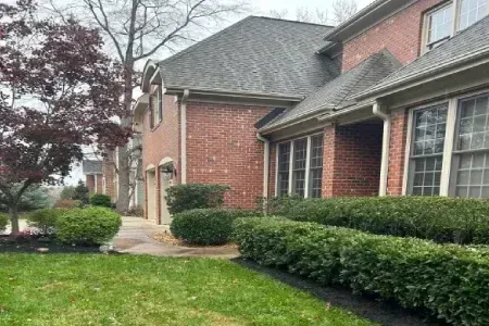 Red brick house with a dark roof and green hedges in front. Cloudy day.