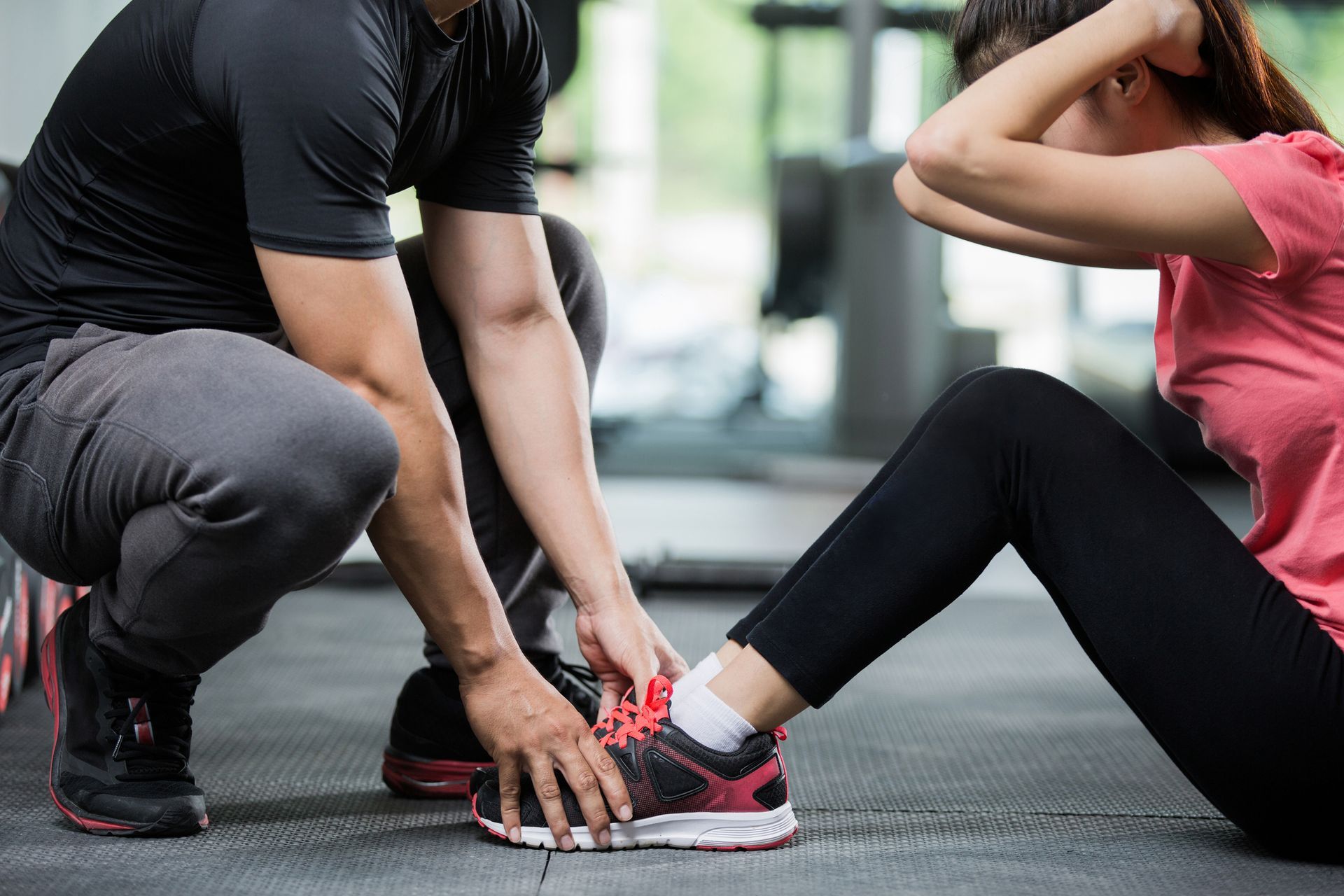Un hombre está ayudando a una mujer a hacer abdominales en un gimnasio.