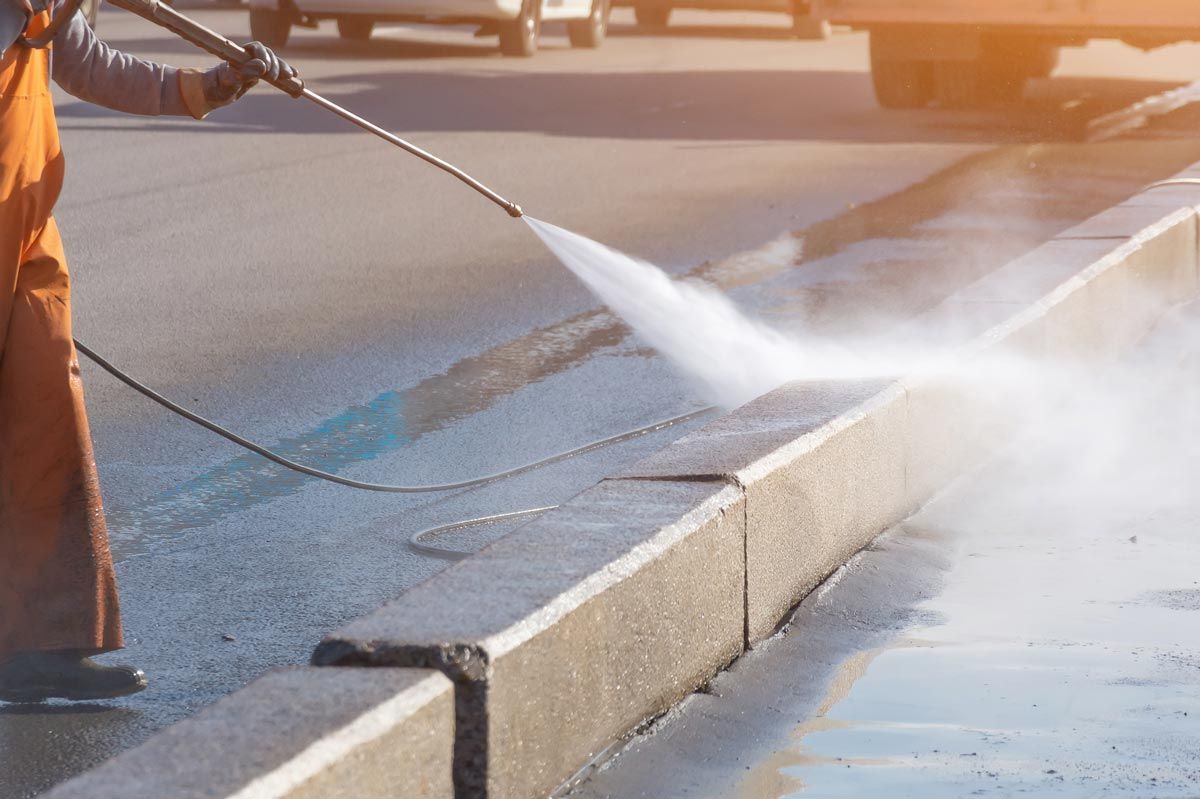 A man is using a high pressure washer to clean the sidewalk.