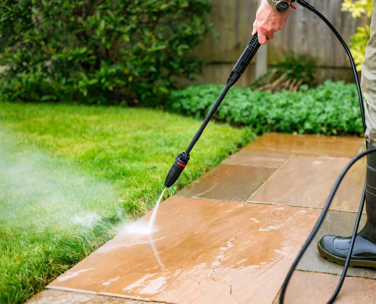 A man is using a high pressure washer to clean a patio.