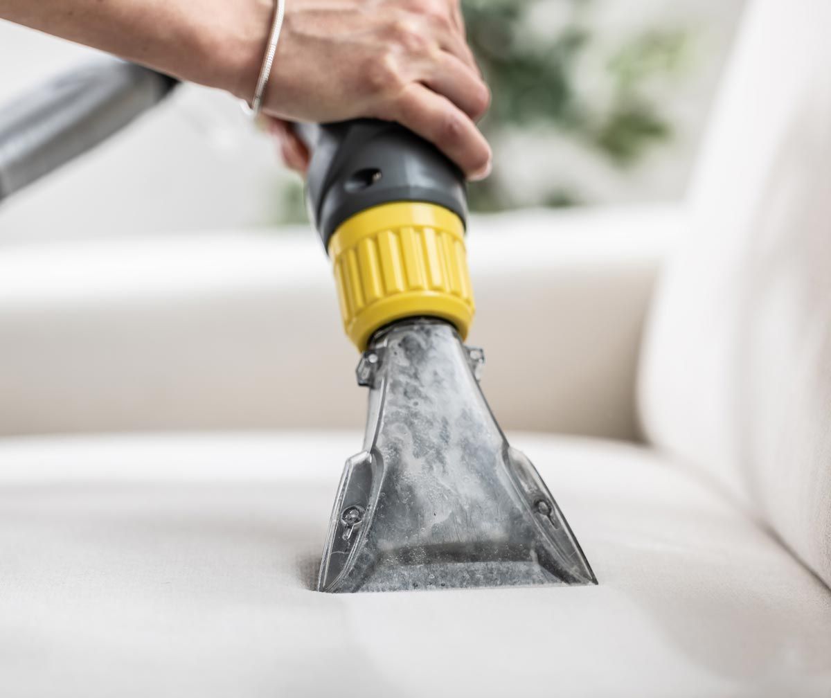 A person is cleaning a couch with a vacuum cleaner.