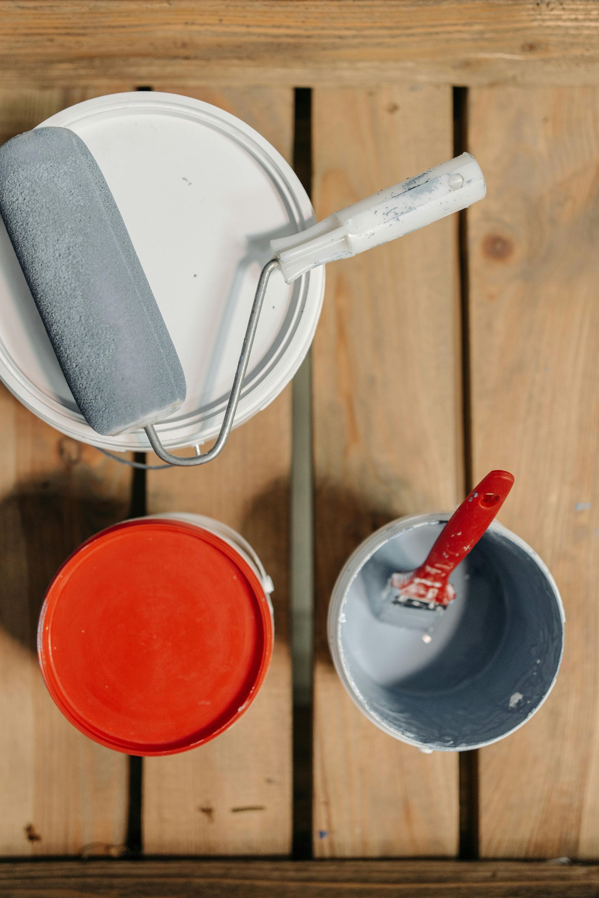 Three buckets of paint and a paint roller on a wooden table