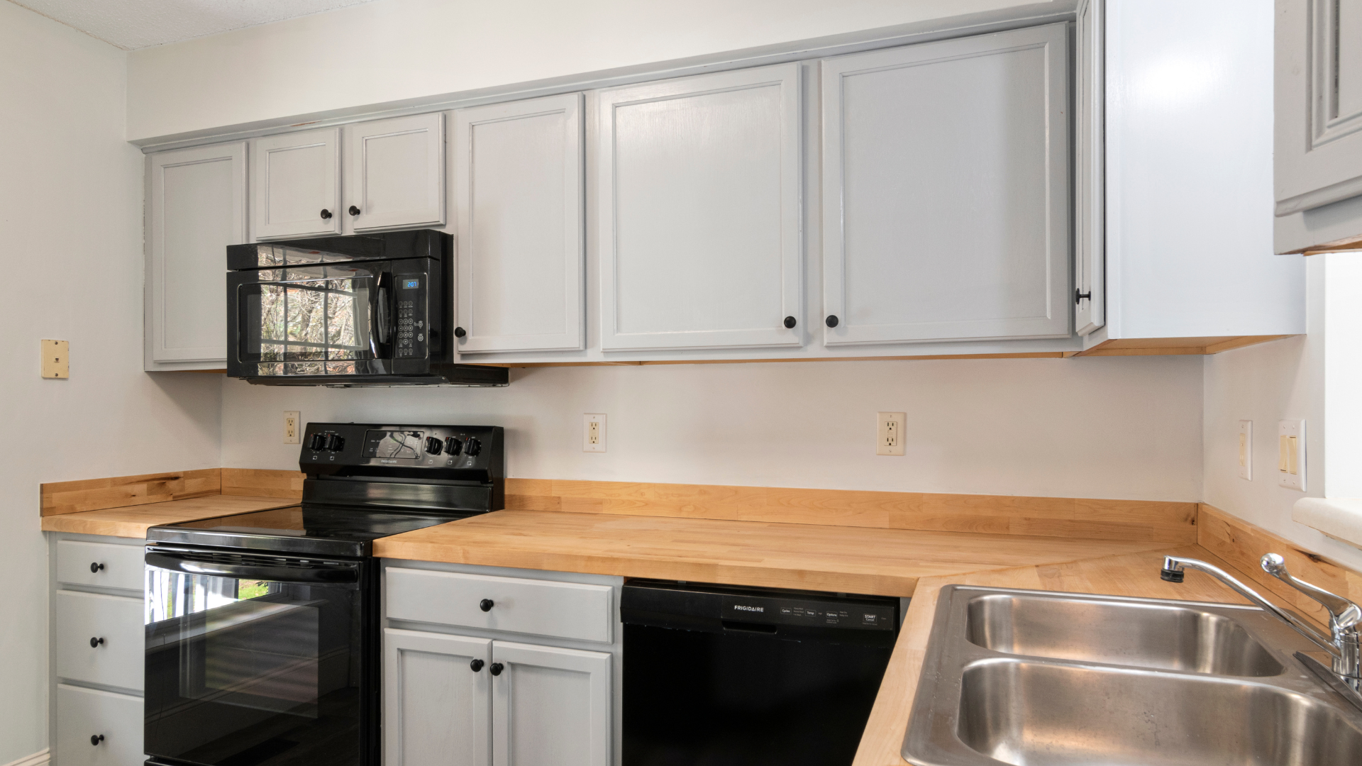 A kitchen with white cabinets , a stove , a sink , and a microwave.