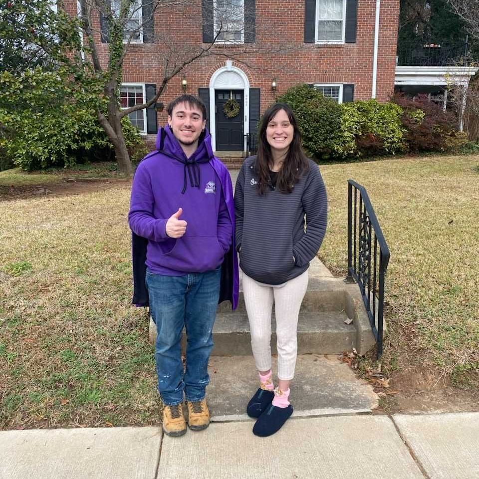 A man in a purple hoodie is giving a thumbs up next to a woman