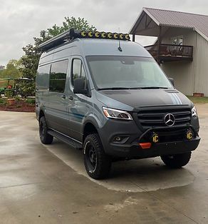 A mercedes van is parked in a parking lot in front of a house.