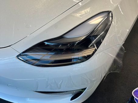 A white tesla model 3 is wrapped in plastic.