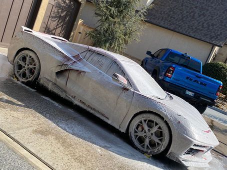 A car is covered in foam and is parked in front of a house.