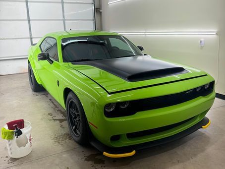 A green dodge challenger with a black hood is parked in a garage.