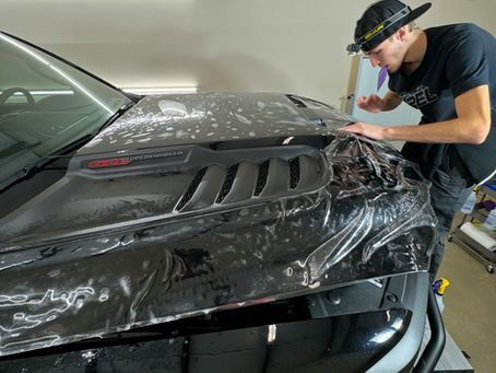 A man is covering the hood of a car with plastic wrap.
