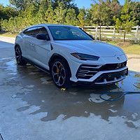 A white lamborghini urus is being washed with a hose.
