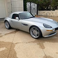 A silver sports car is parked in a driveway next to a garage.