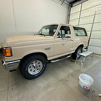 A white ford bronco is parked in a garage next to a bucket.