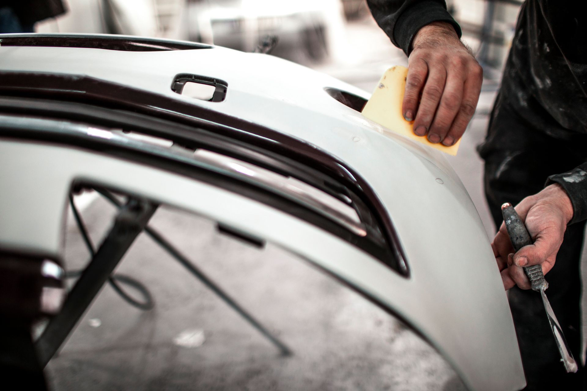 A man wearing a mask is spray painting a car in a garage.