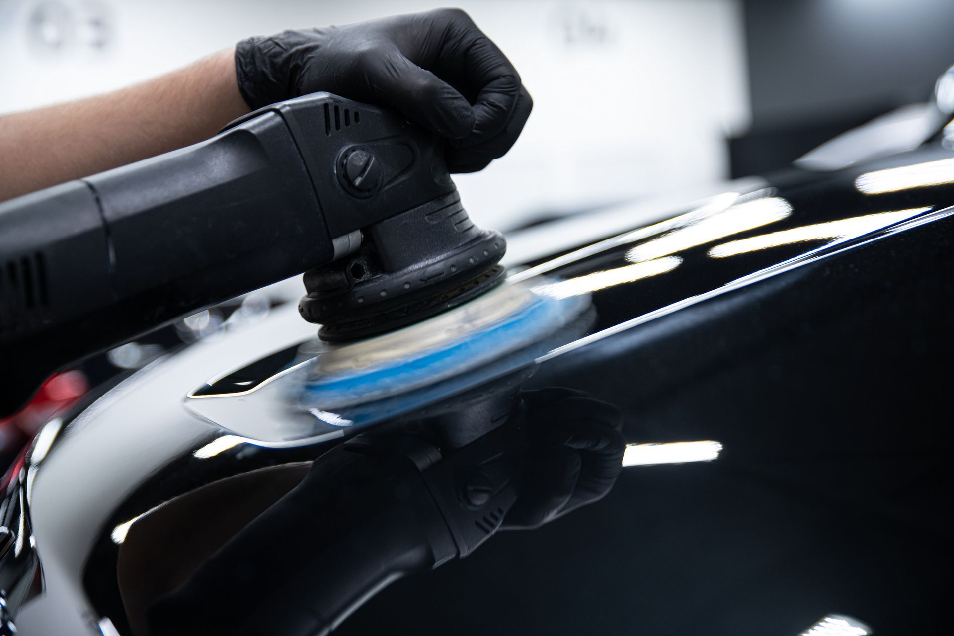 A person is polishing a black car with a machine.