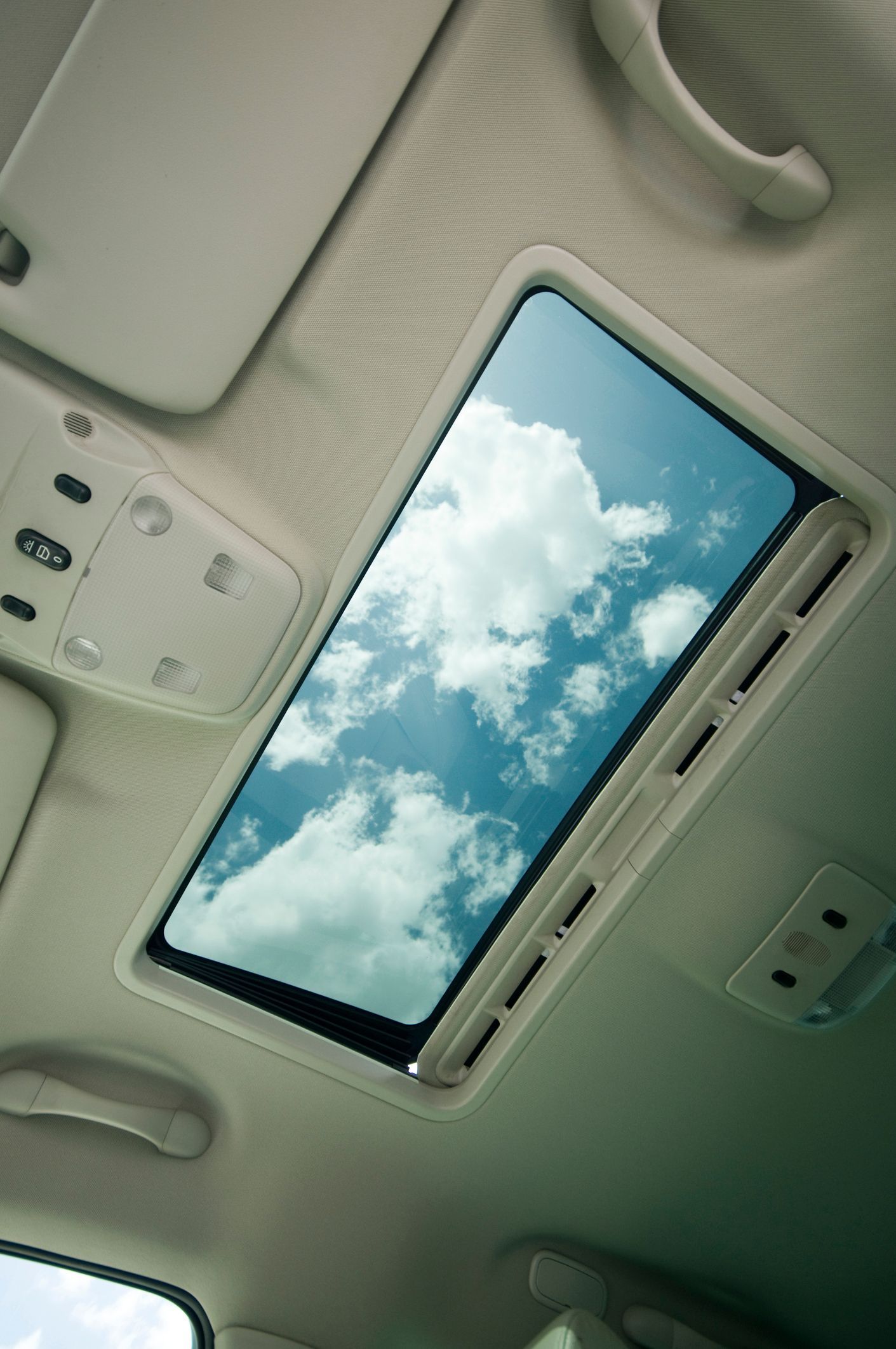 The sunroof of a car shows a blue sky with white clouds