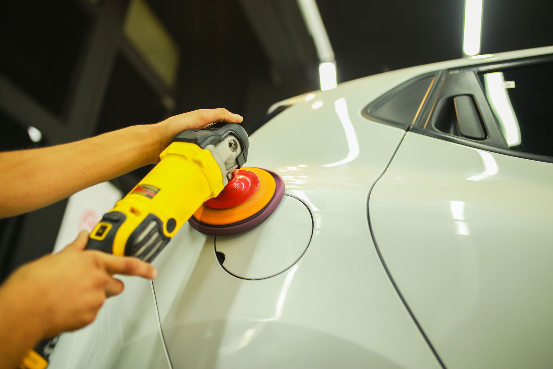A person is polishing a white car with a yellow and orange machine.