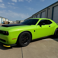 A bright green dodge challenger is parked in front of a garage.