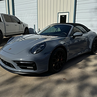 A gray porsche 911 cabriolet is parked in front of a garage.