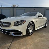 A white mercedes benz s class convertible is parked in front of a garage.