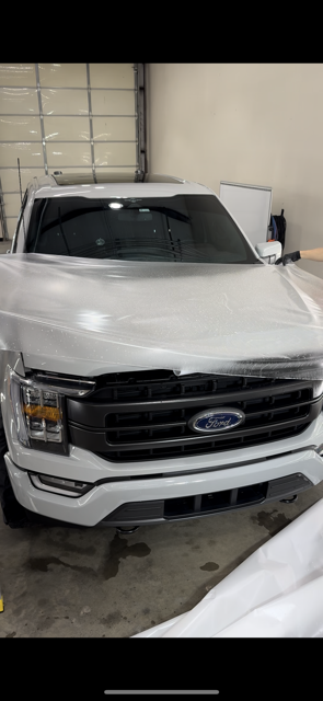 A white Ford F-150 pickup truck in a garage. The front of the truck is visible, with its grille and headlights.