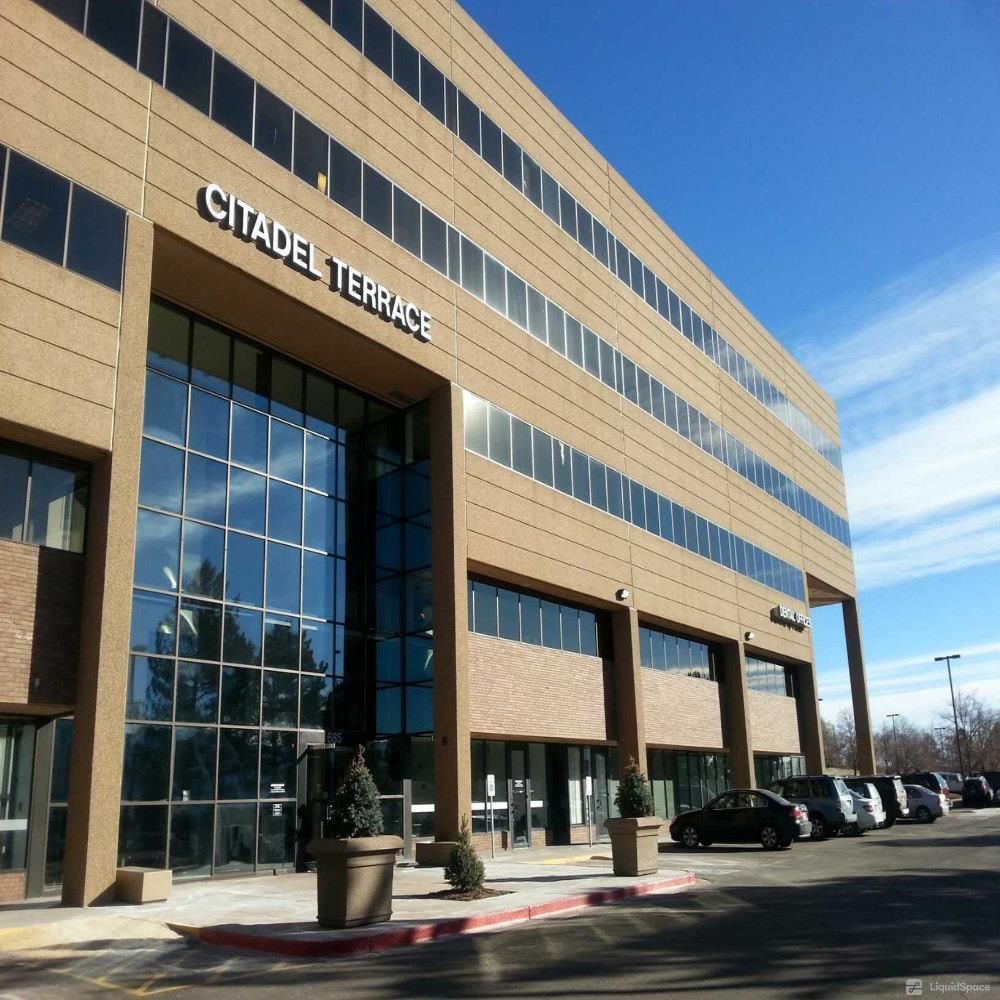 Edificio de oficinas Citadel Terrace con una gran entrada acristalada, exterior marrón y coches aparcados. Cielo azul.