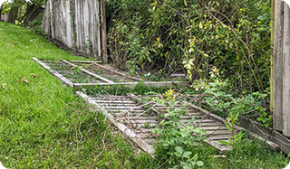 a broken wooden fence is sitting in the grass next to a wooden fence .