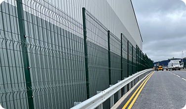A fence is along the side of a highway next to a building.