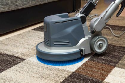 Carpet cleaner machine scrubbing a patterned rug, next to a sofa. Carpet cleaner machine scrubbing a patterned rug, next to a sofa.