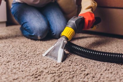 Person using carpet cleaner on beige carpet, wearing gloves.