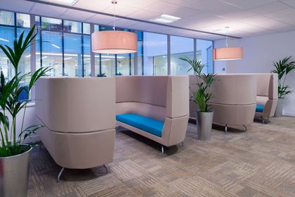 Modern office lounge area with tan booths, turquoise seating, and potted plants. Modern office lounge area with tan booths, turquoise seating, and potted plants.
