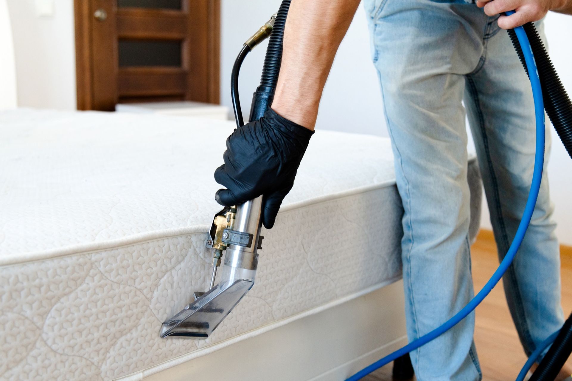 Person cleaning a white mattress with a professional vacuum, indoors.