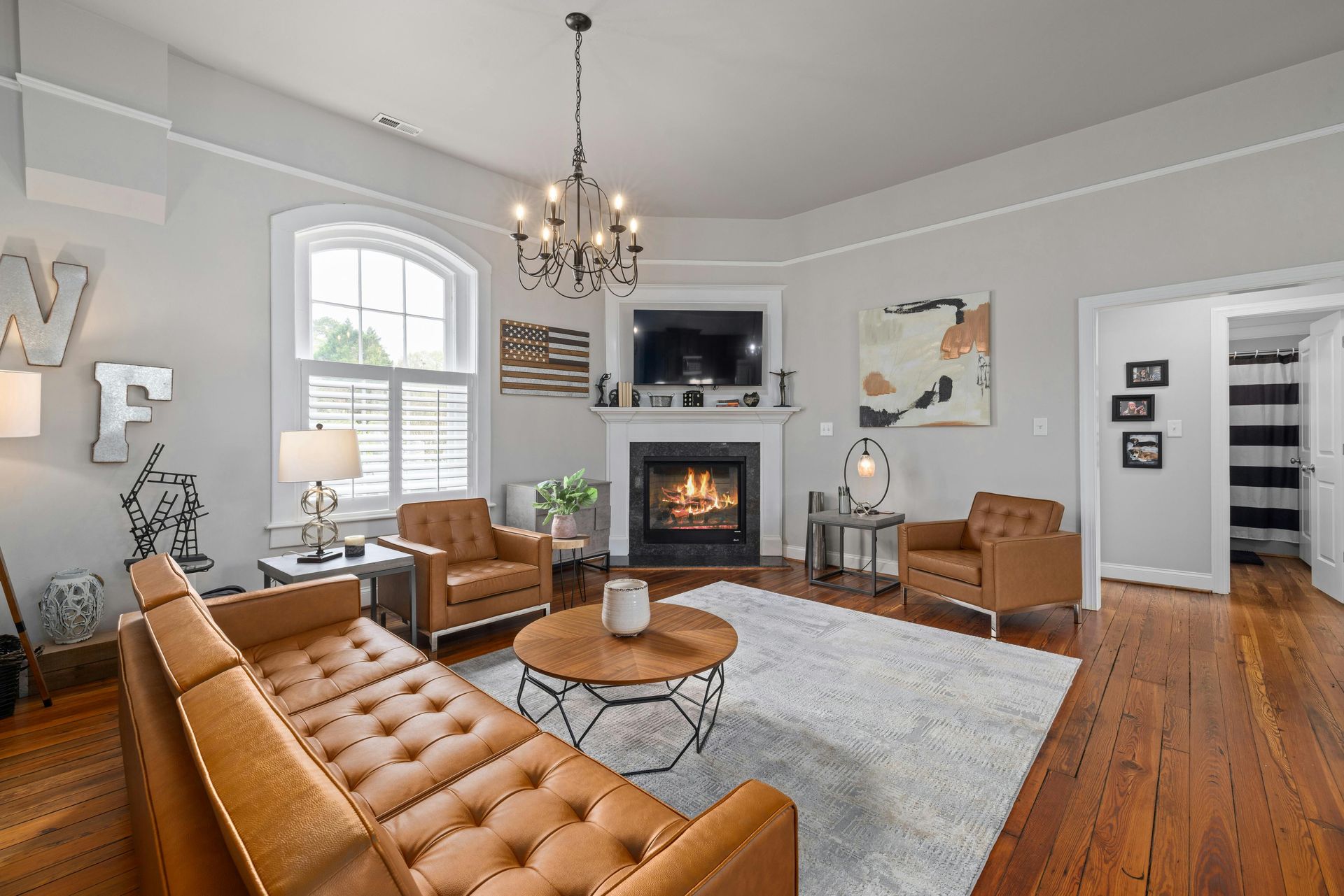 Living room with brown leather furniture, fireplace, chandelier, and hardwood floors.