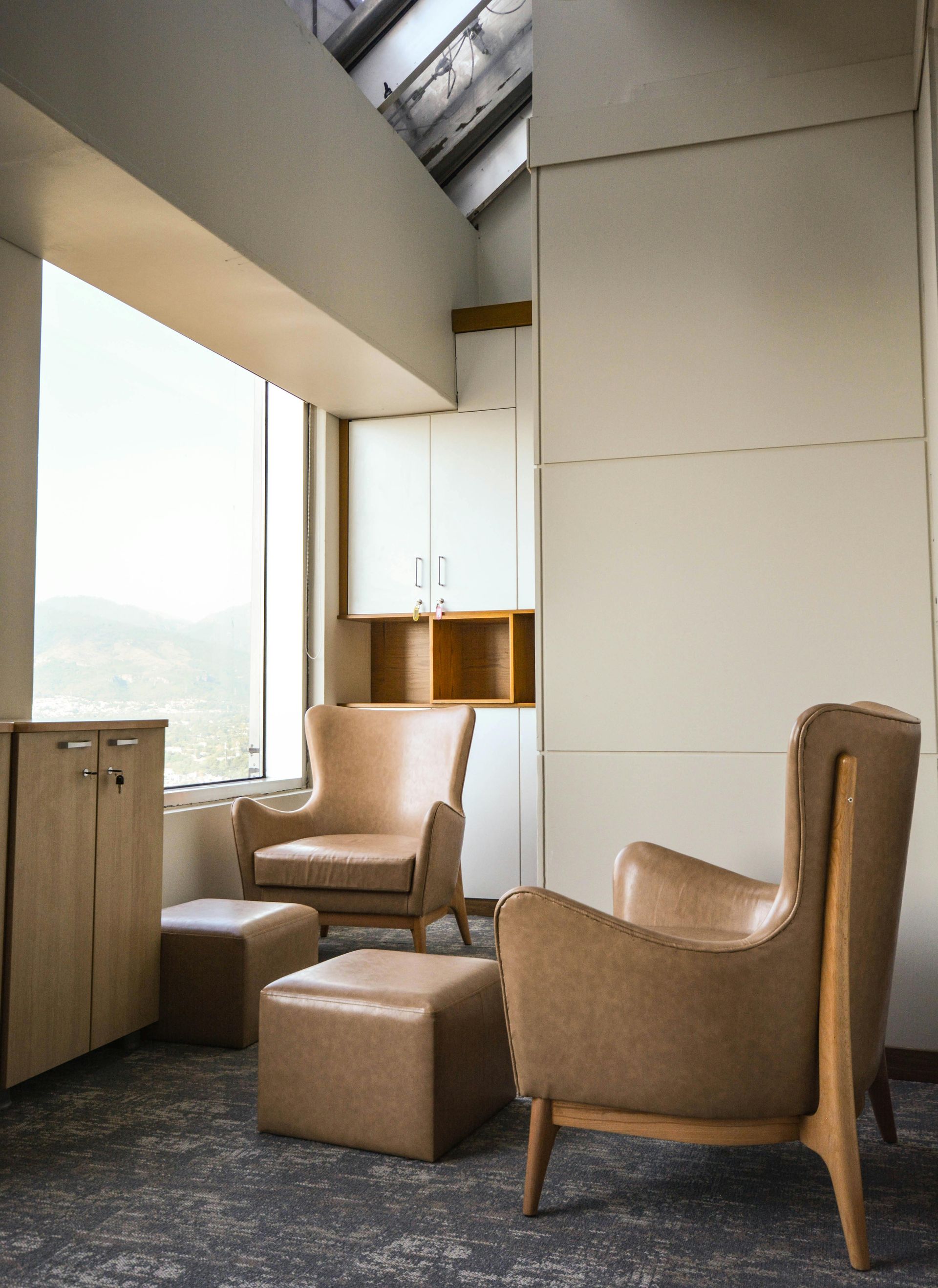 Living room with two tan leather armchairs and ottomans. Large window with mountain view.