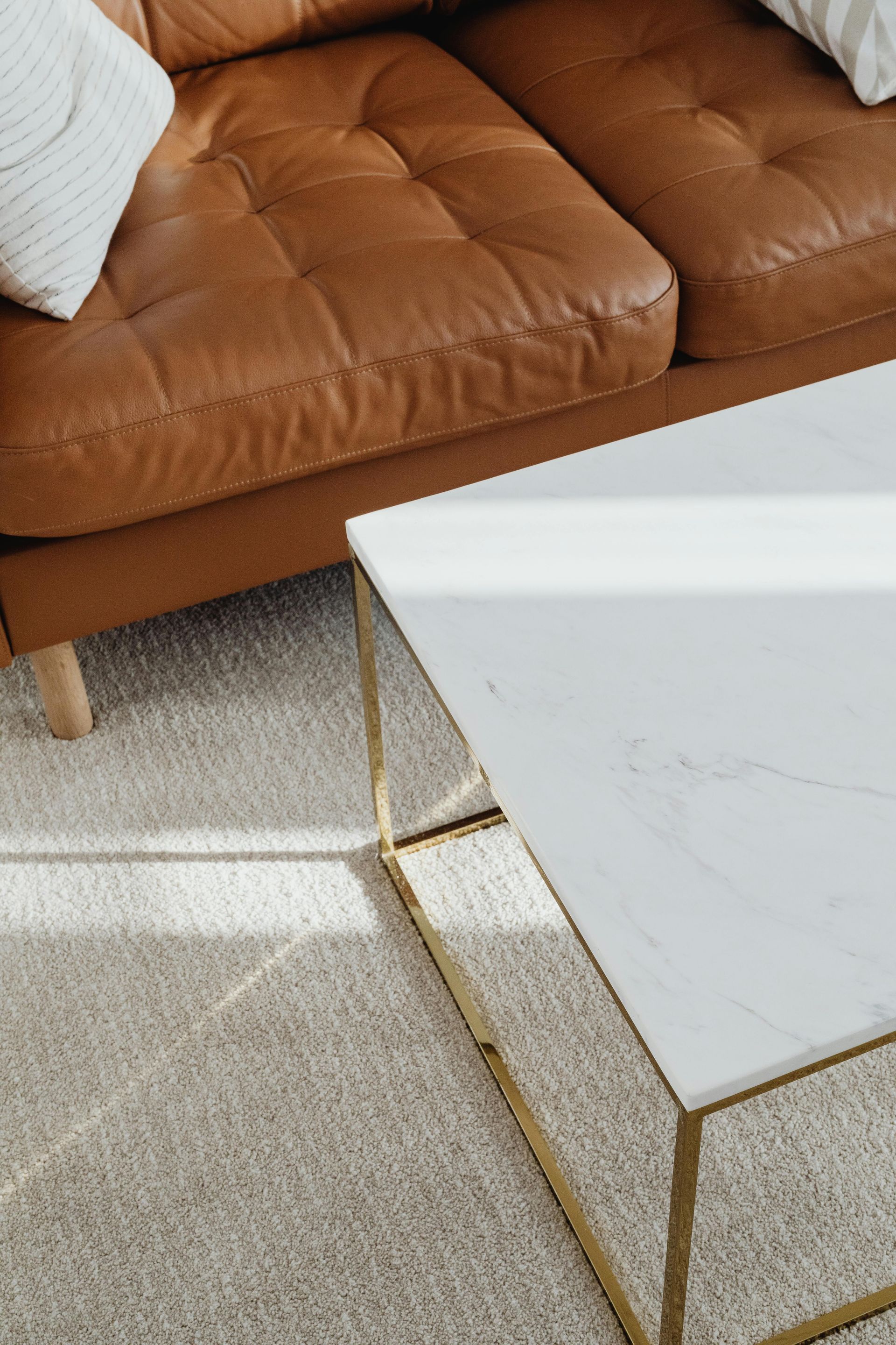 Brown leather couch next to a white marble coffee table on a beige rug.