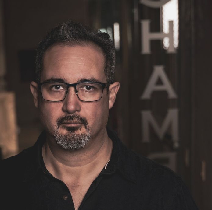 A man with glasses and a beard stands in front of a sign that says ham