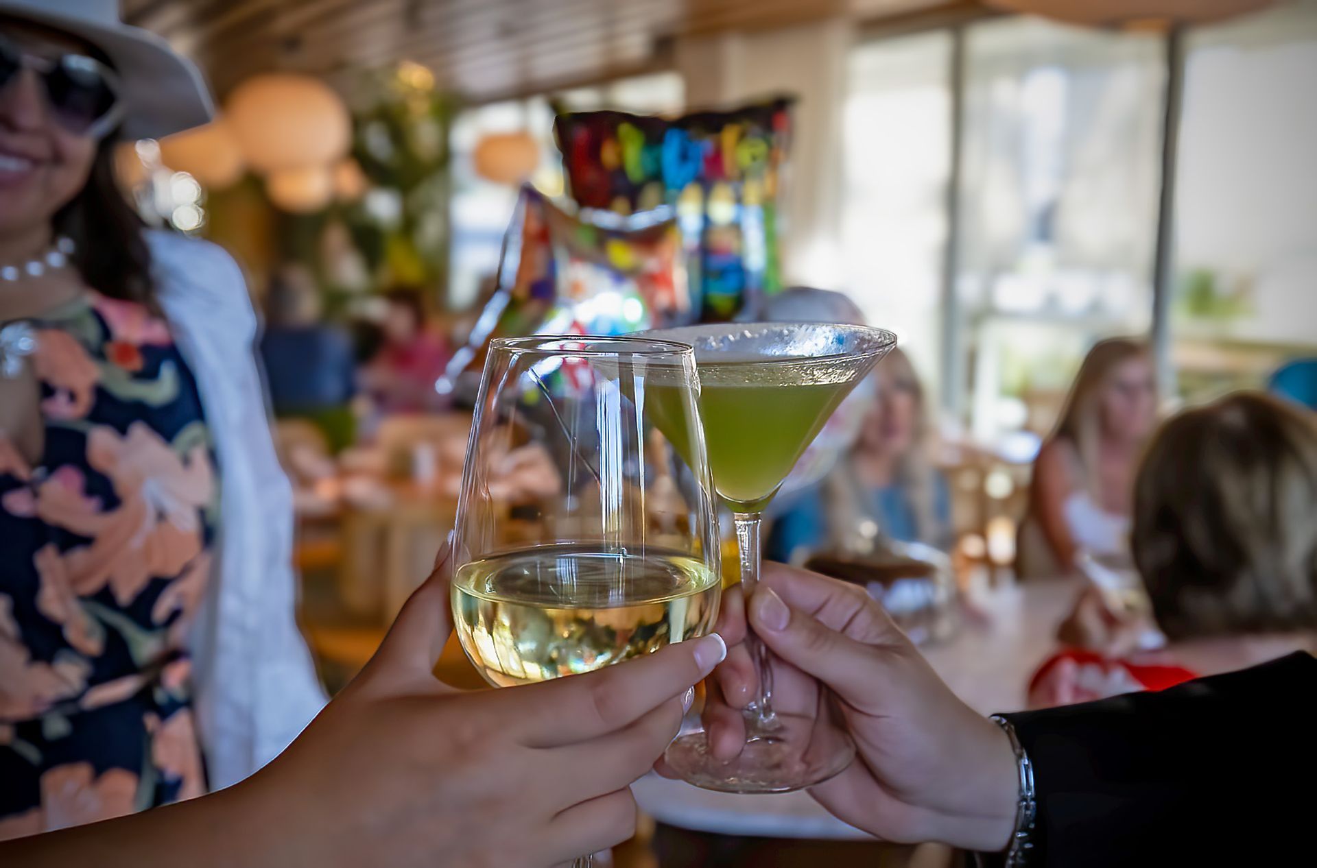 People toasting with wine glasses at a restaurant, with other diners in the background.