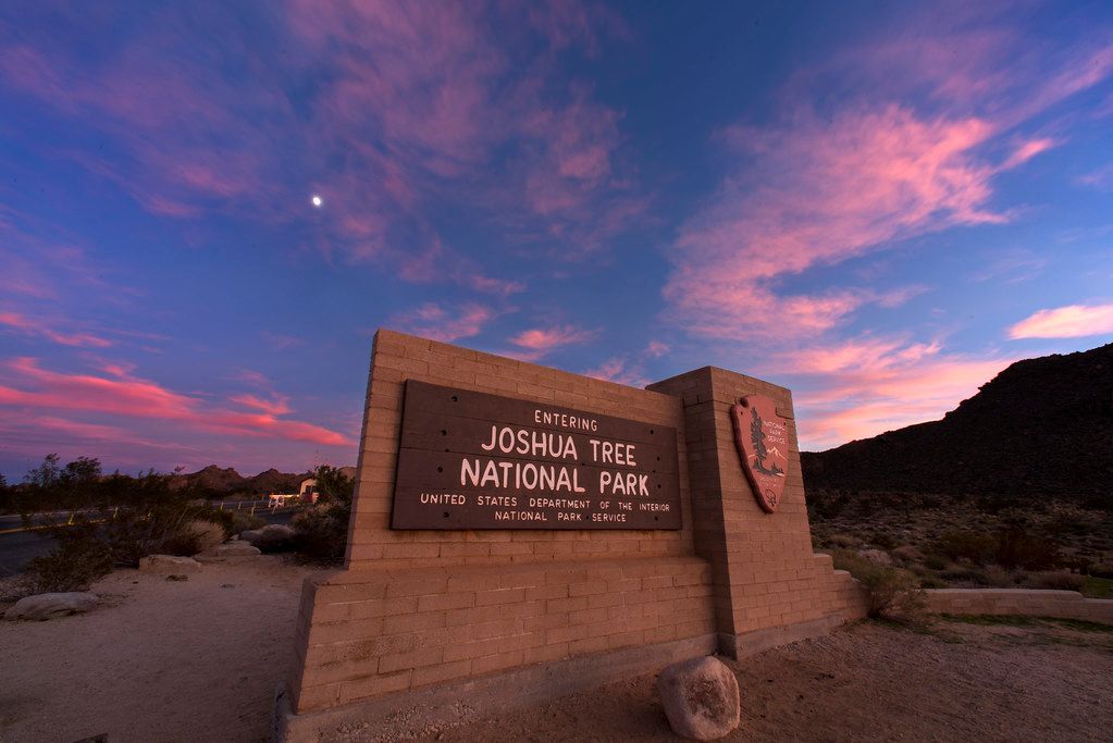 A sign for joshua tree national park with a sunset in the background.