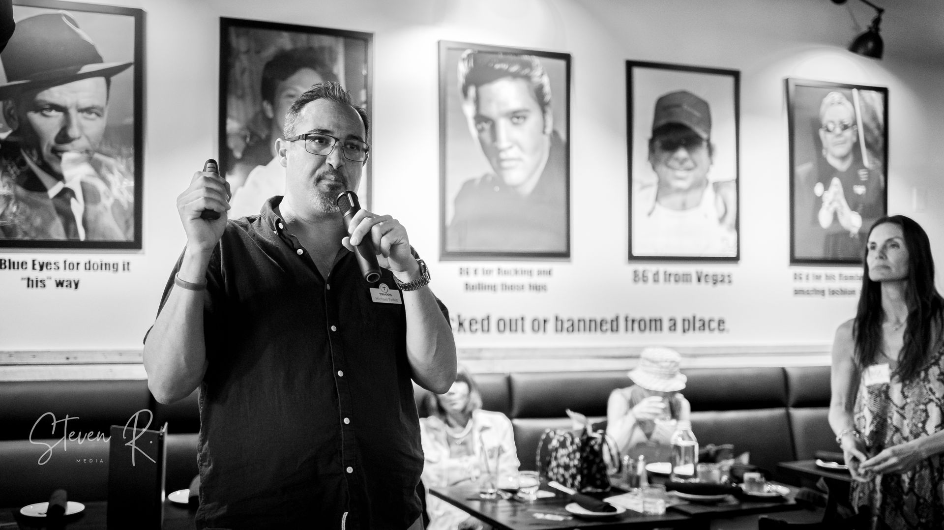 A man is holding a microphone in front of a group of people in a restaurant.