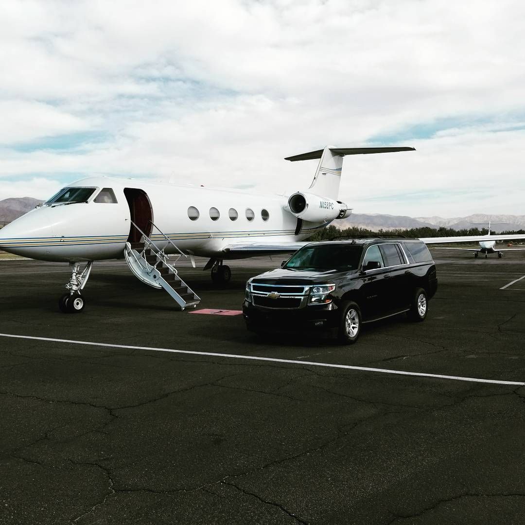 A black suv is parked next to an airplane on a runway