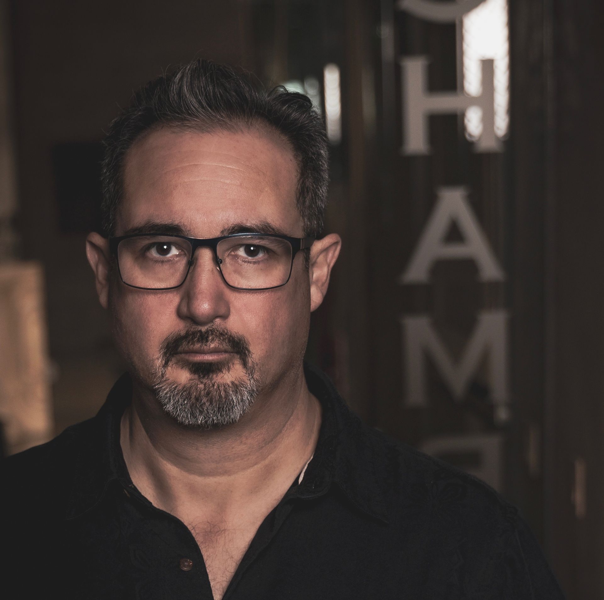 A man with glasses and a beard stands in front of a sign