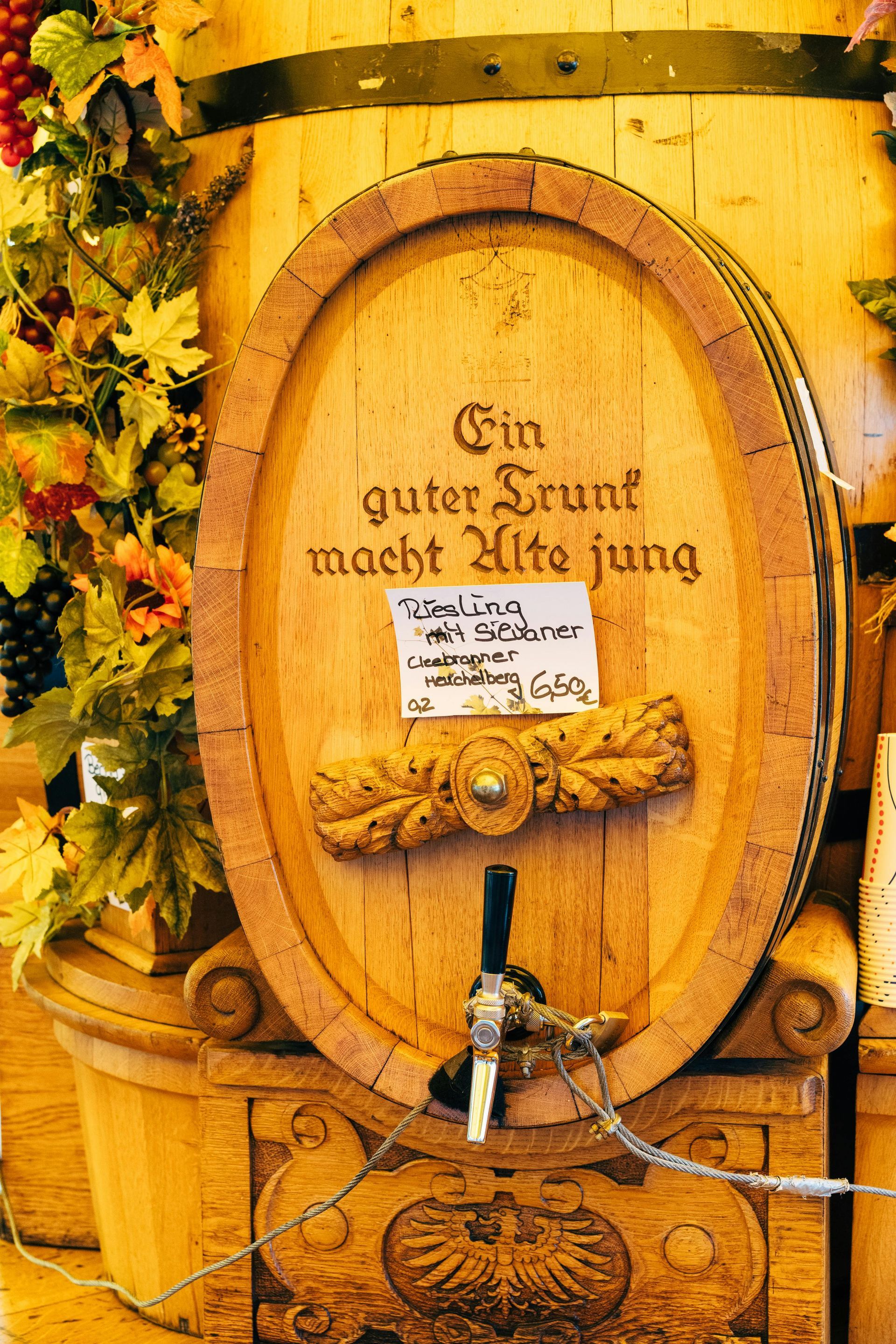 Wooden barrel with text and tap, decorated with foliage.