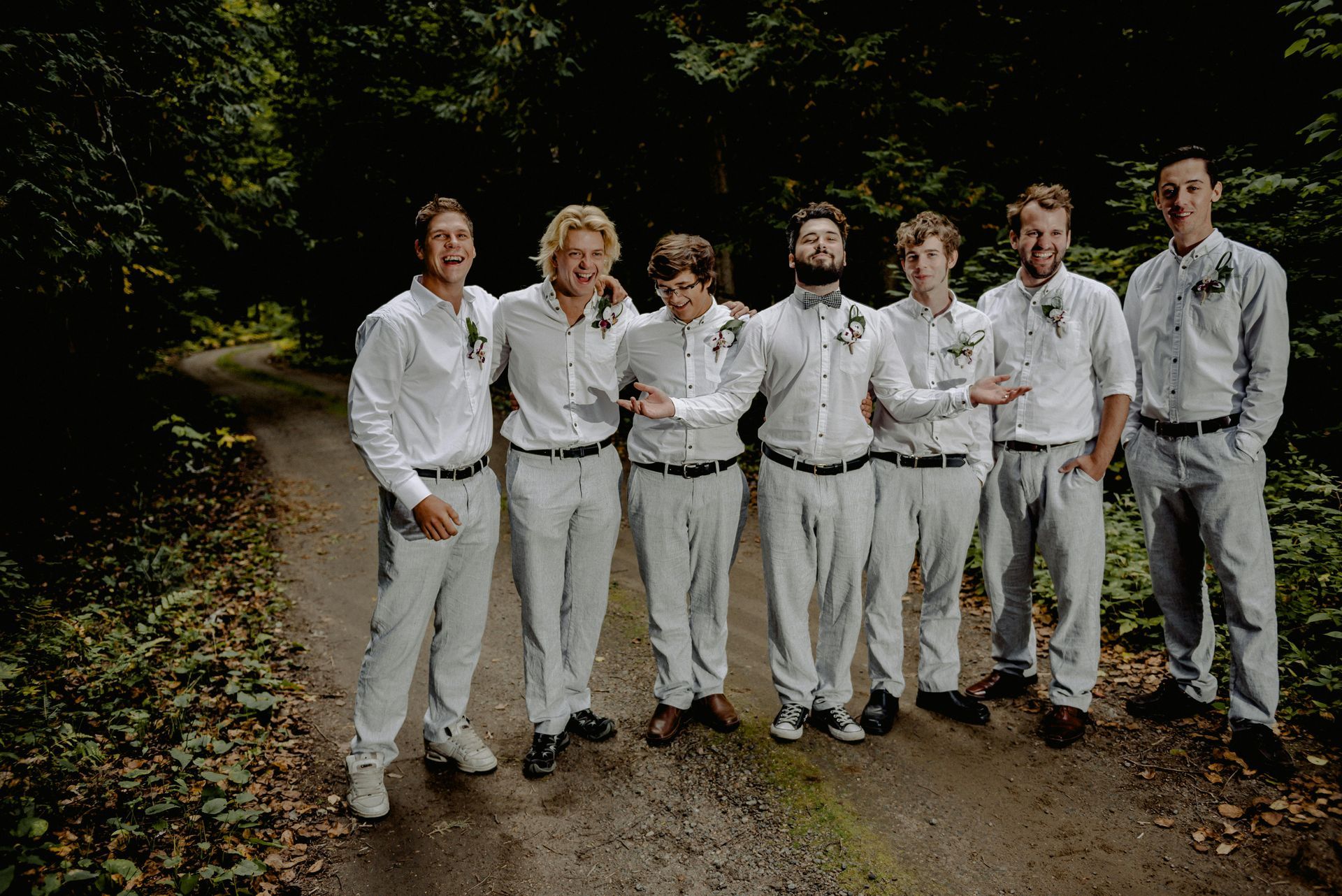 A group of men in white shirts and pants are standing next to each other on a dirt road.