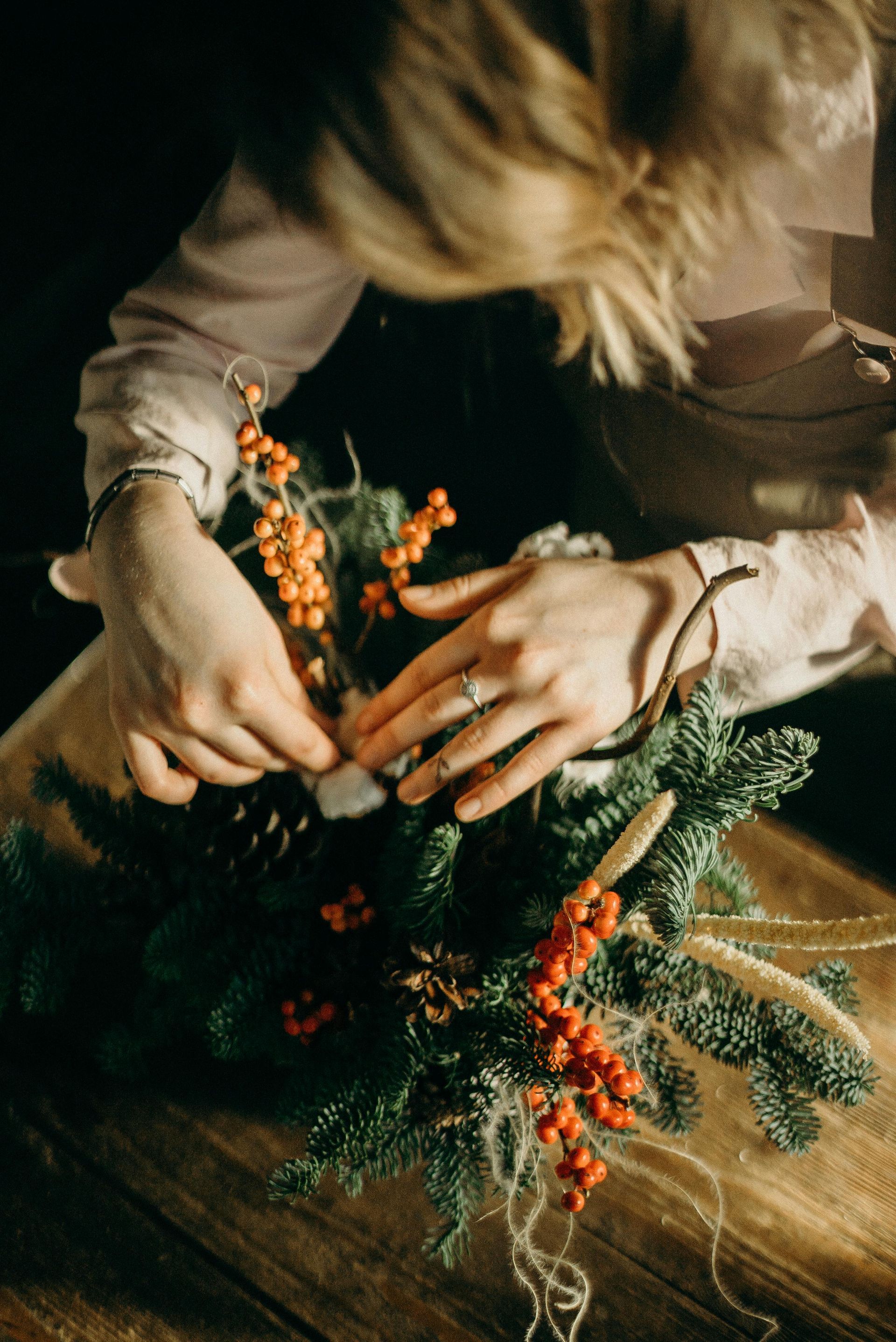 A woman is making a christmas wreath with berries and pine cones.