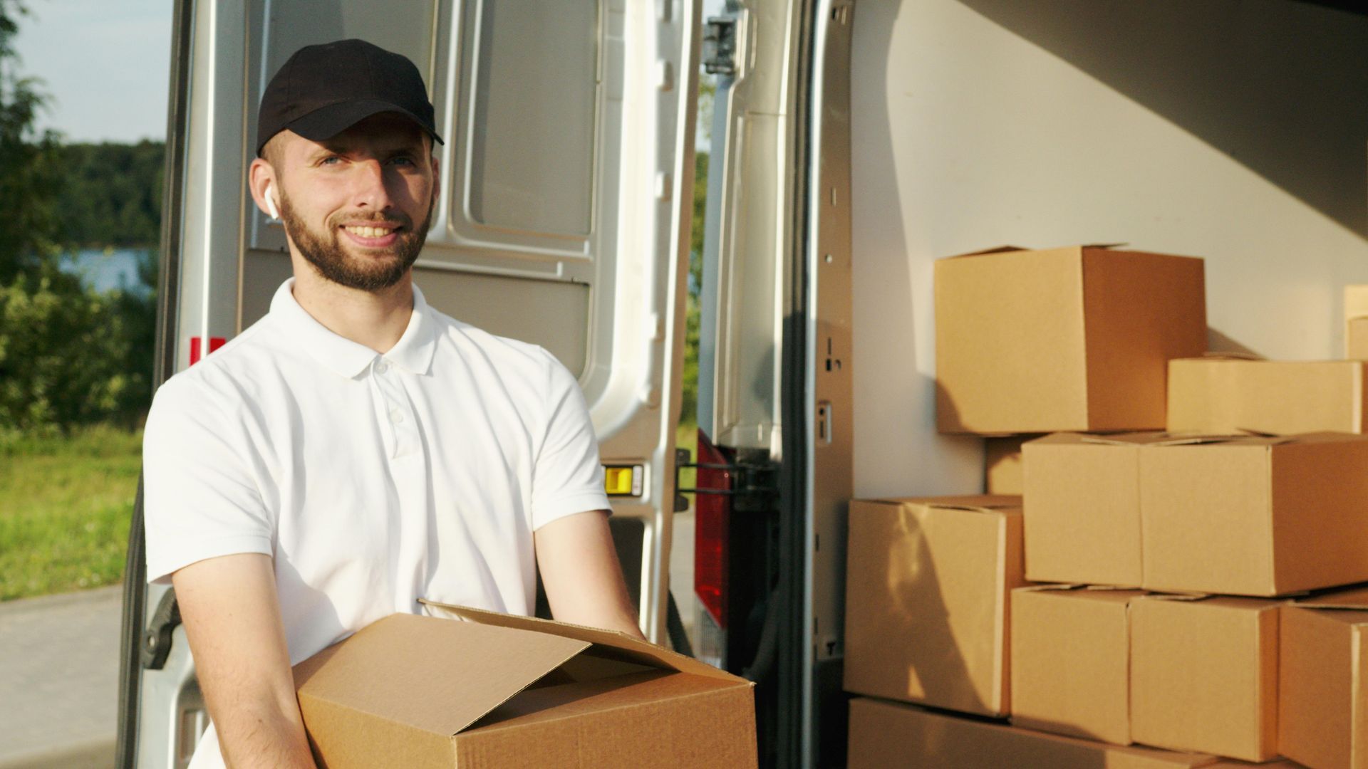 A delivery man is holding a cardboard box in front of a van.