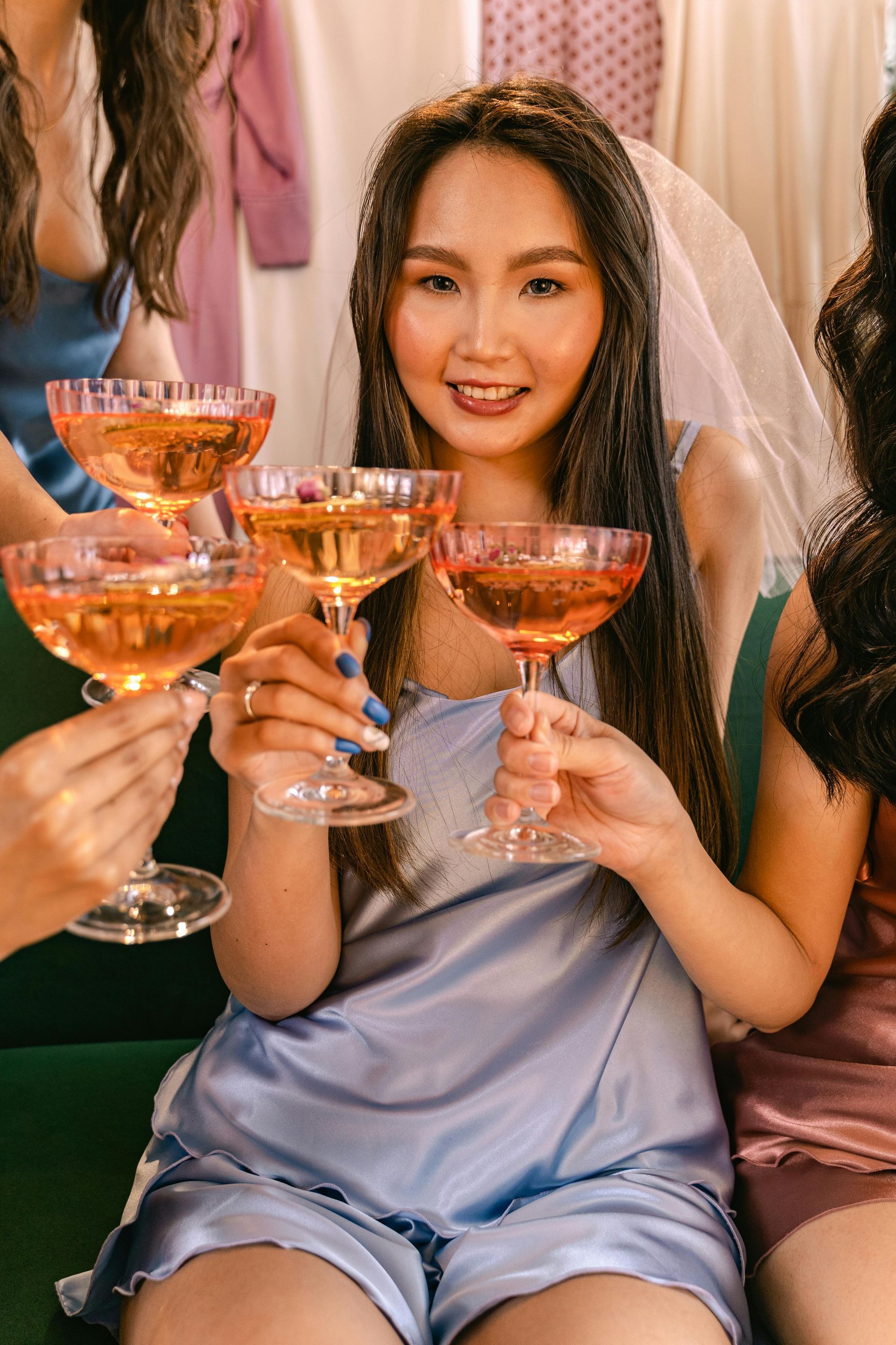 Woman in blue pajamas, holding a glass of orange champagne, surrounded by others, a bridal veil, celebration.