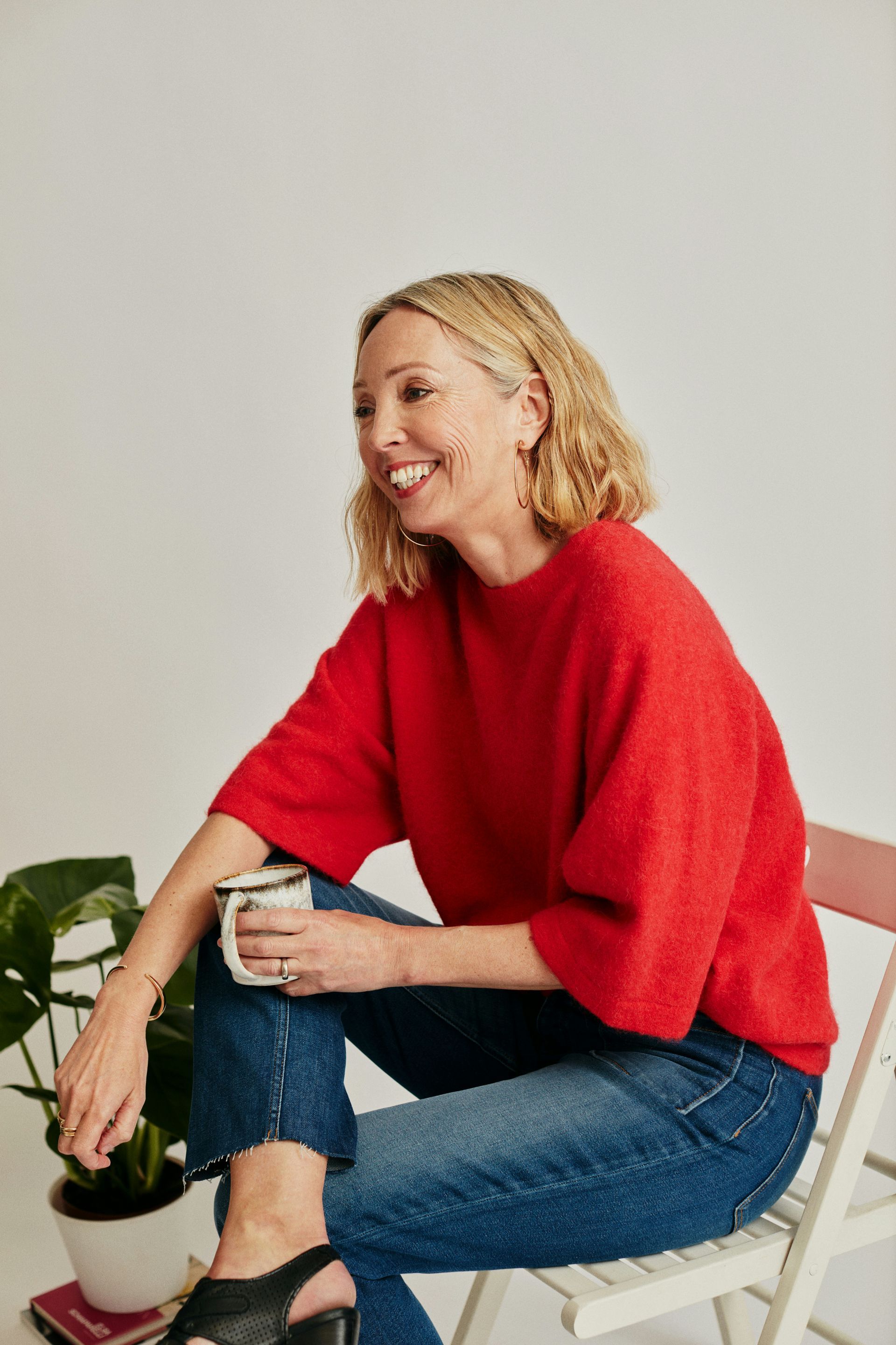 A woman in a red sweater is sitting on a chair holding a cup of coffee.