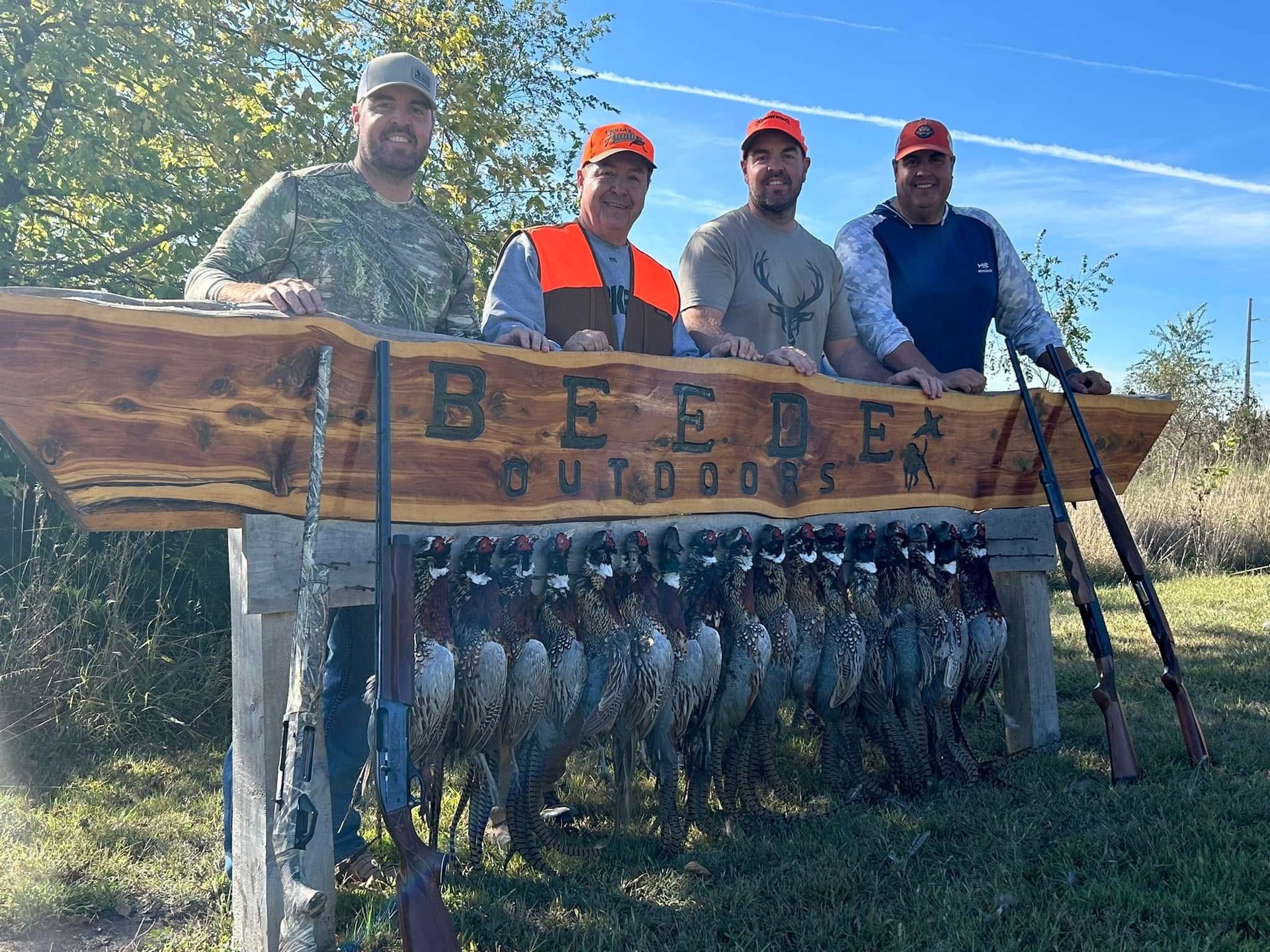 Four hunters pose with shotguns and harvested pheasants beneath a 