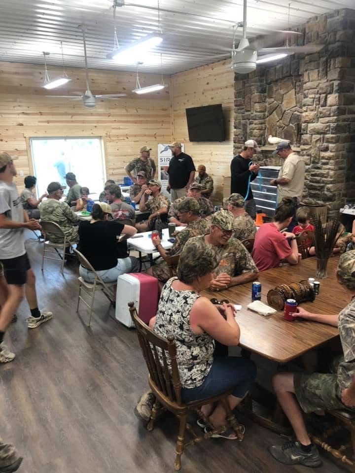 People seated around tables in a lodge, some in camouflage. Gathering.