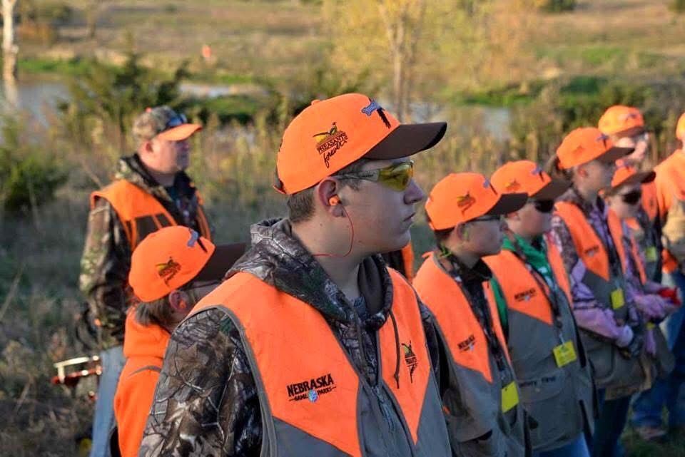 Group of people in orange vests and hats, waiting outdoors.